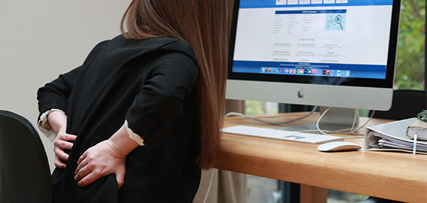Woman sitting at a computer holding back in pain 